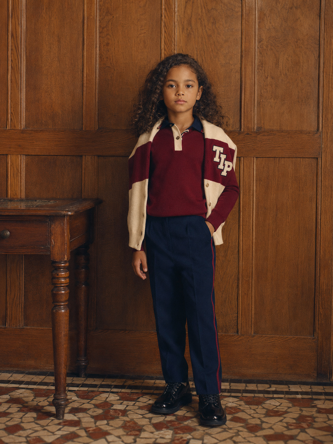 Child in TIP varsity knitwear against oak panelling